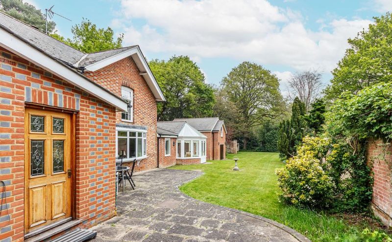 A brick and timber porch beside a paved drive, with the lawn and garden room beyond.