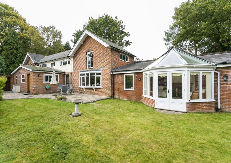 The rear elevation of the house seen across the lawn, with a glazed garden room to one side.