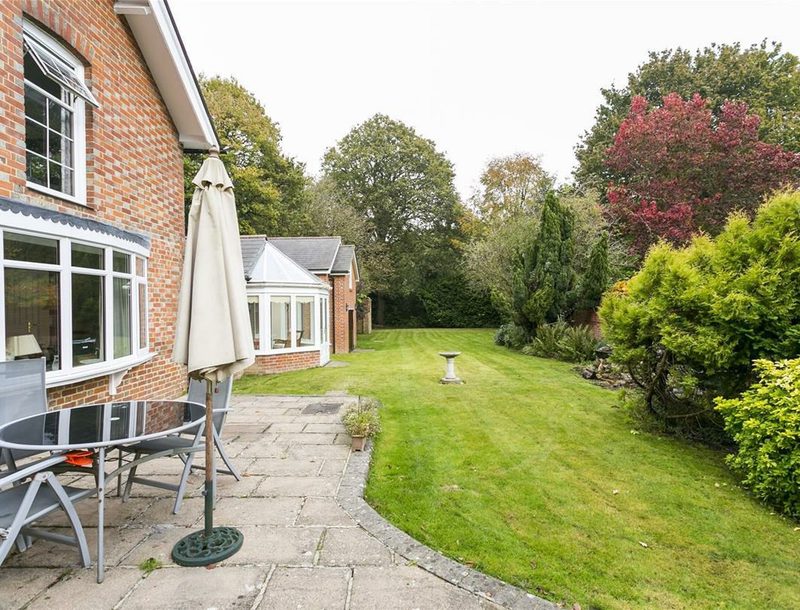 A paved terrace with a table, chairs and a parasol beside the brick house.